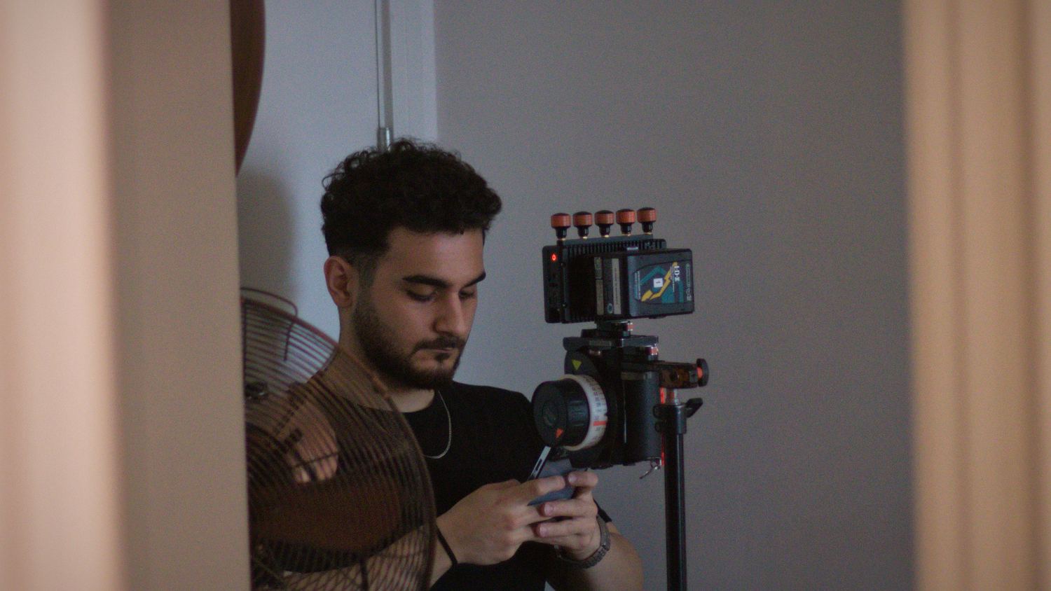 A crew member checking the camera beside a bright curtained window on set